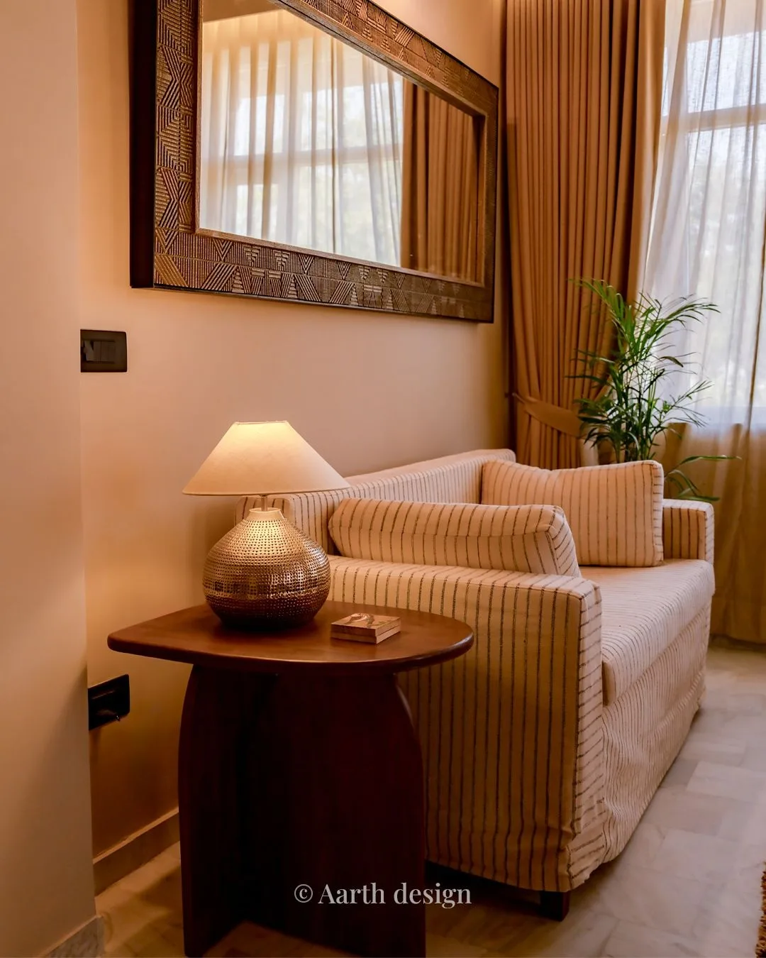 Side table and a hammered-brass lamp beneath a carved mirror, beside the striped sofa