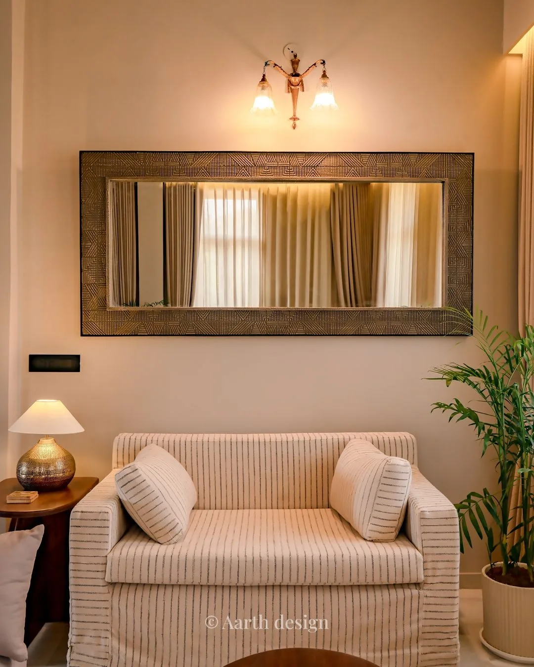 Striped loveseat set beneath a tall brass-framed mirror and wall sconce