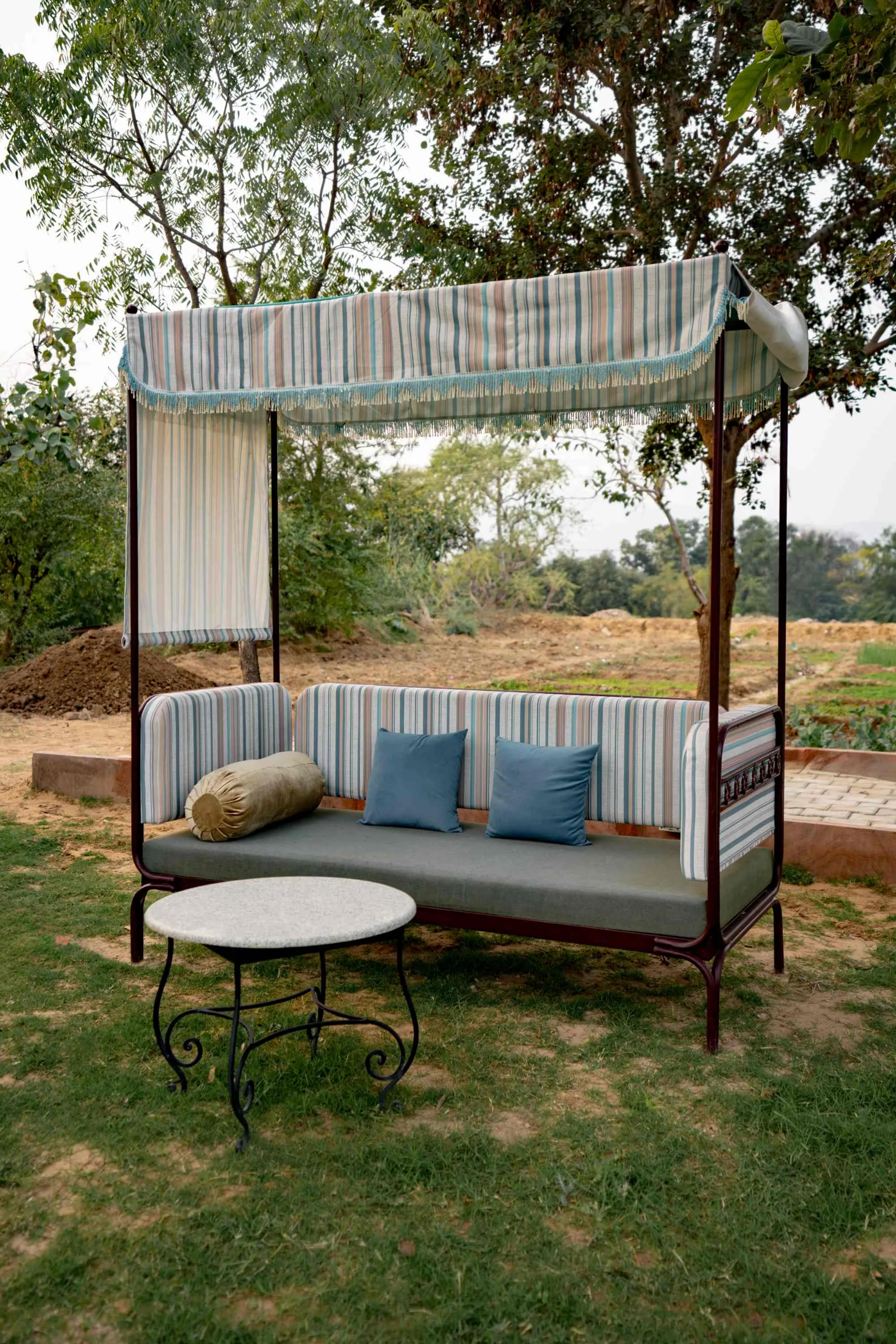 A canopied daybed on the lawn, with the Aravalli hills beyond