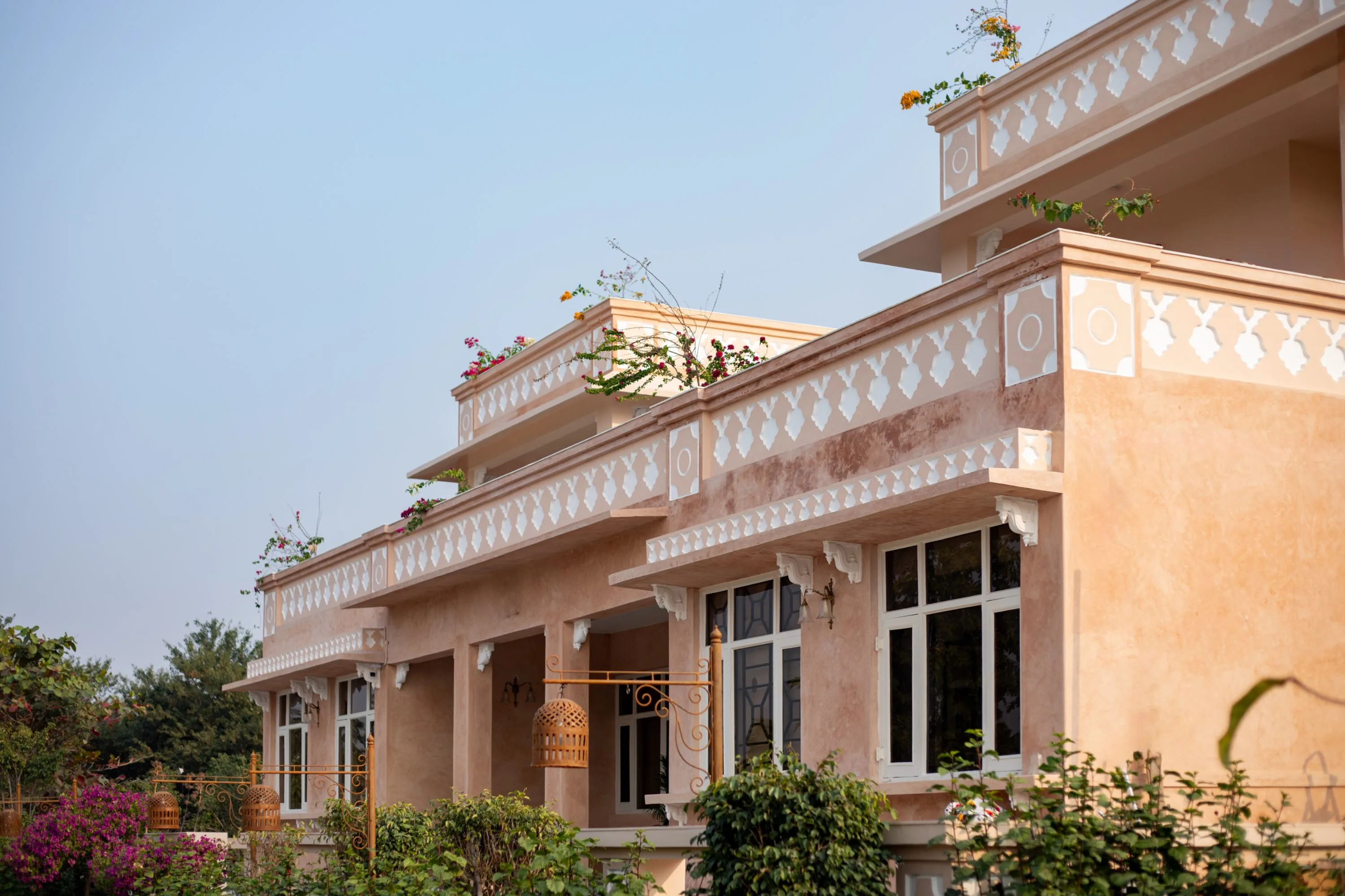 Wide view of the pink stucco facade with its carved jaali balustrade and bougainvillea