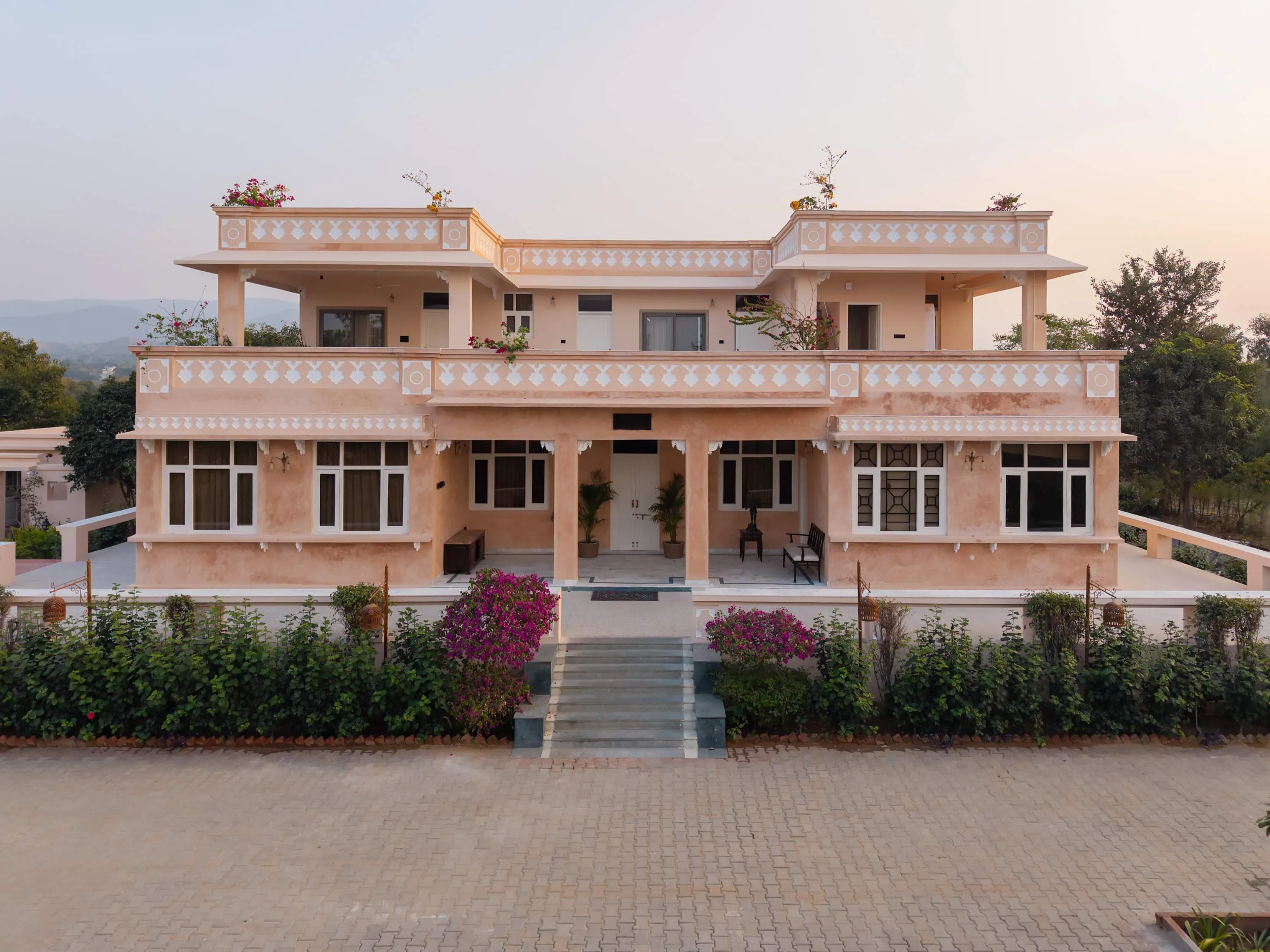 Full front elevation of the retreat at golden hour, with stone steps and bougainvillea leading to the veranda