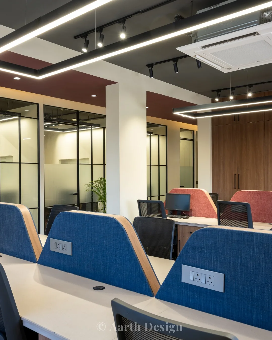 Open-plan workstations in blue and coral seen through glazed cabin partitions