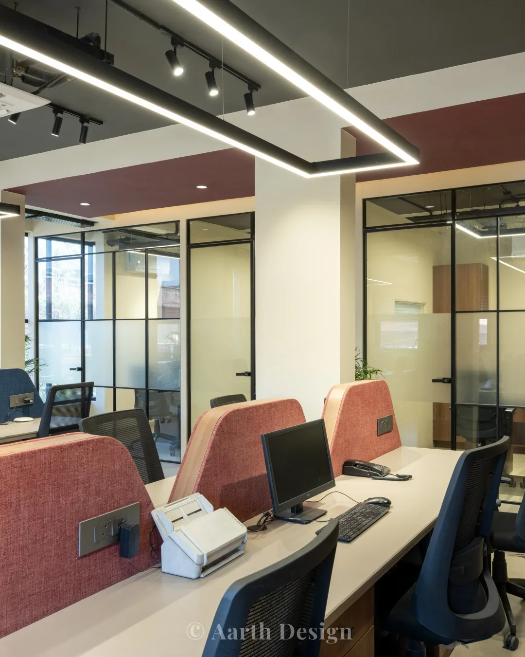 Workstations with coral-backed desks set against glass-fronted cabins