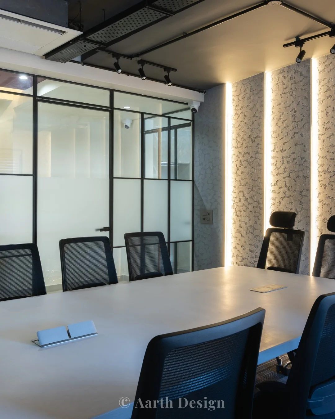 Meeting room behind a black-framed glass partition, beside a lit stone-clad wall