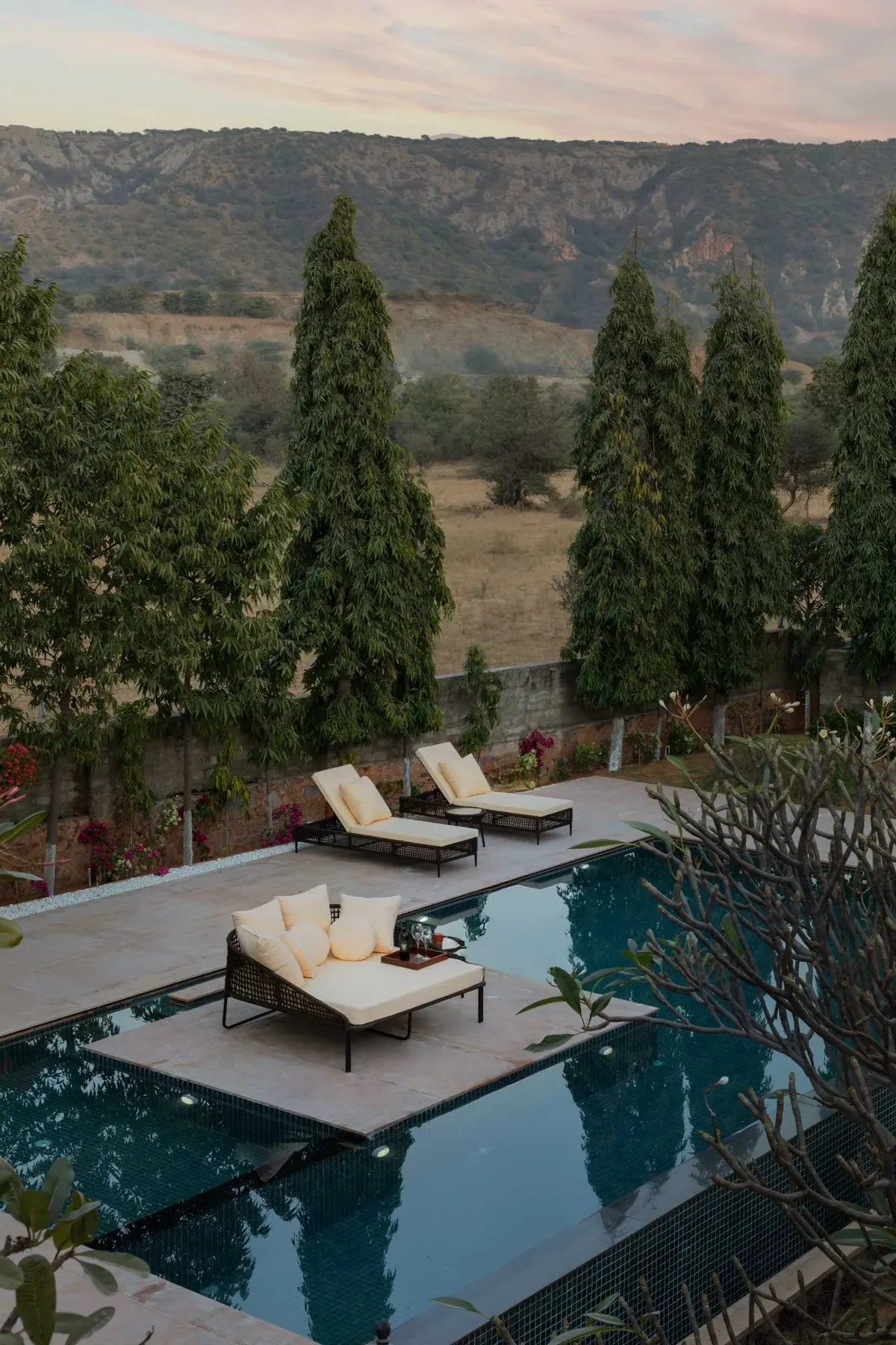 Loungers on a sunken pool deck at dusk, with the Aravalli hills behind