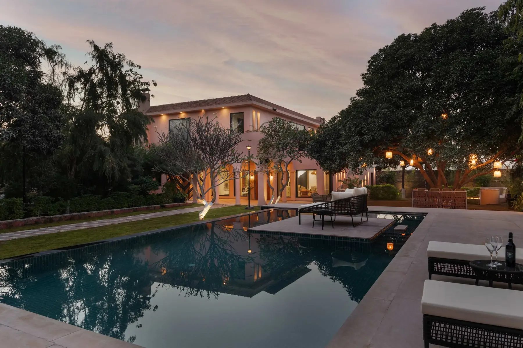 The pool at dusk with the pink stucco house lit warmly behind it
