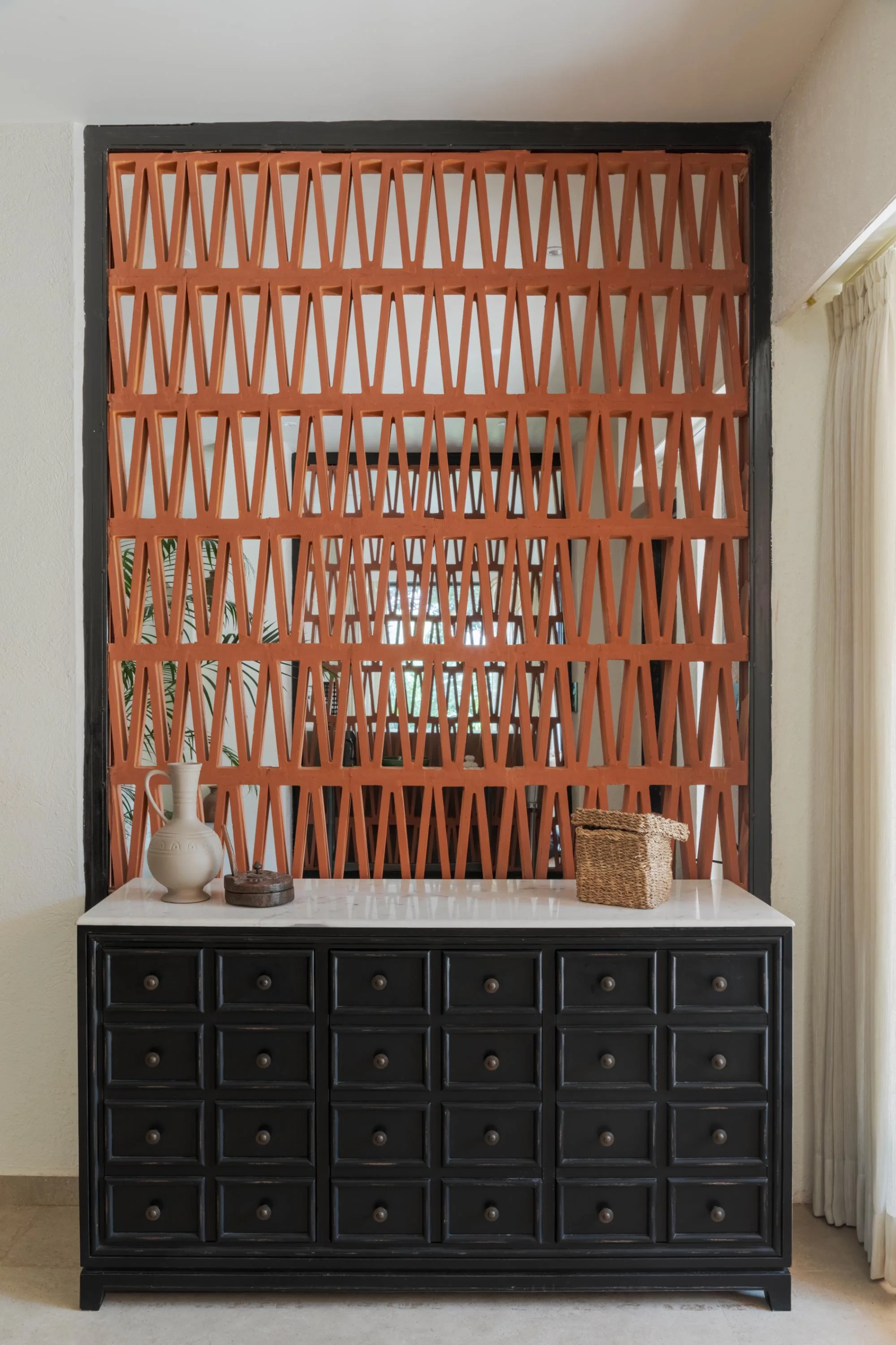 Terracotta jaali screen rising behind a black console with a stoneware jug