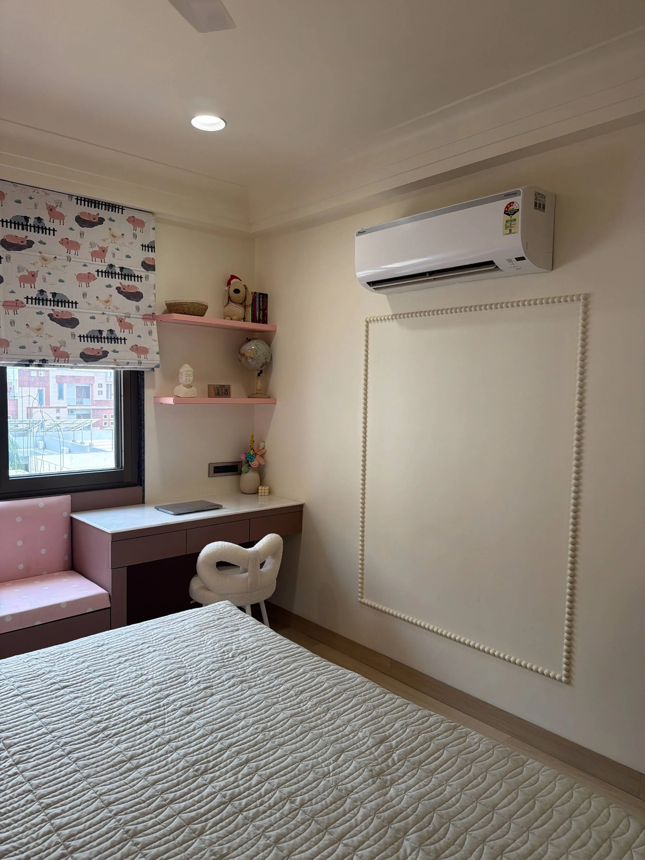 Children's study nook with a pink desk and window seat beneath patterned blinds