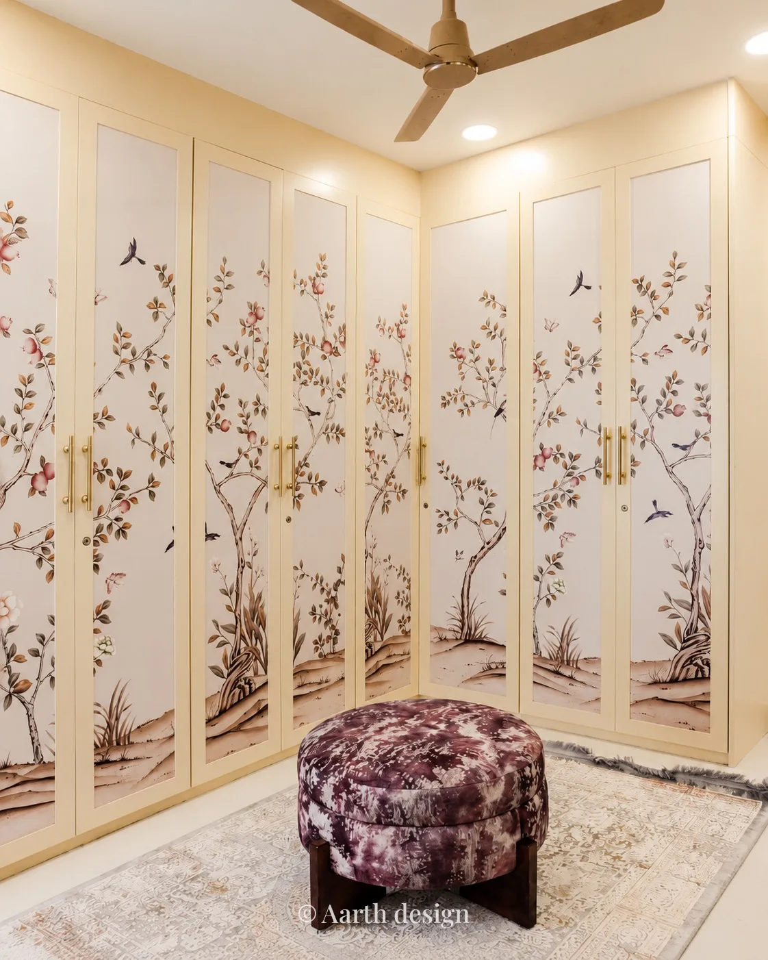 Dressing room lined with botanical-painted wardrobe shutters around a patterned pouffe
